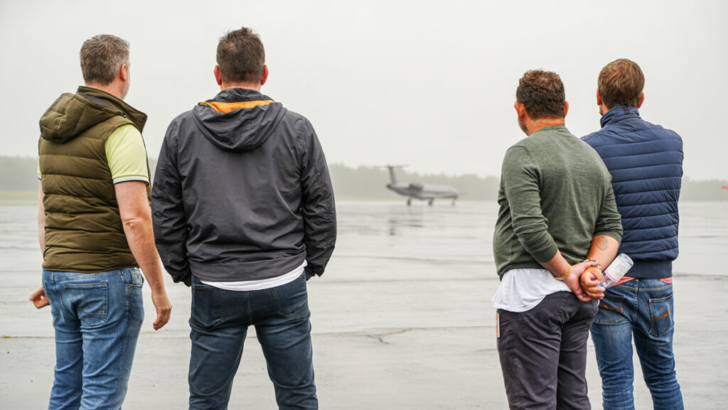 A photo of four men with their back to the camera looking at an airplane on a rainy runway