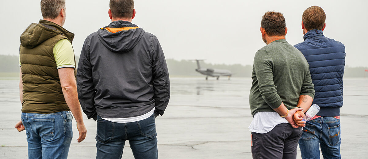 A photo of four men with their back to the camera looking at an airplane on a rainy runway