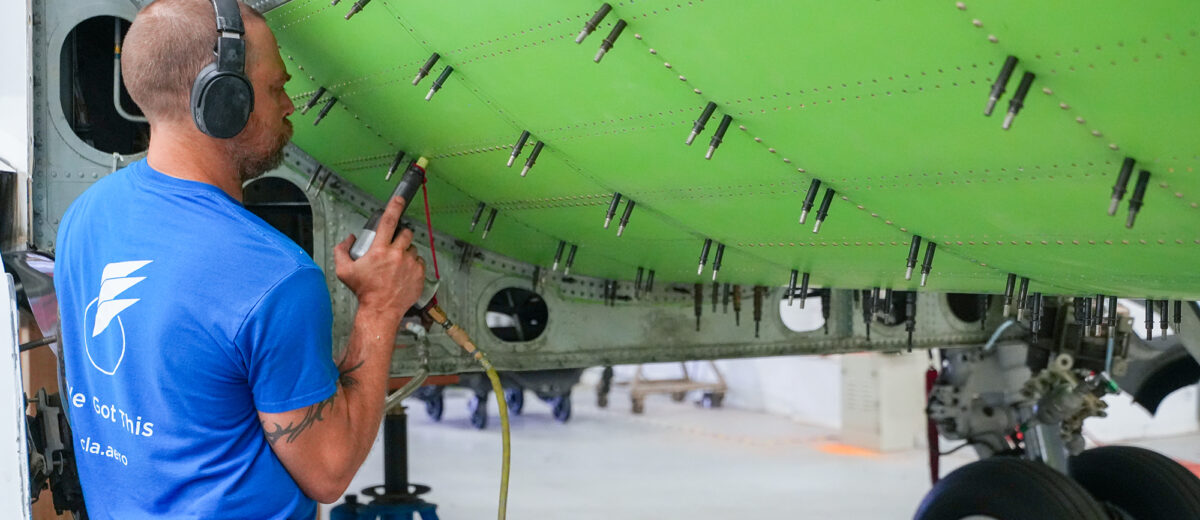 A photo of a mechanic fastening bolts on a bright-green section on the underside of an airplane
